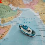 Close-up of a toy boat placed on the Arabian Sea section of a world map depicting regions around India.